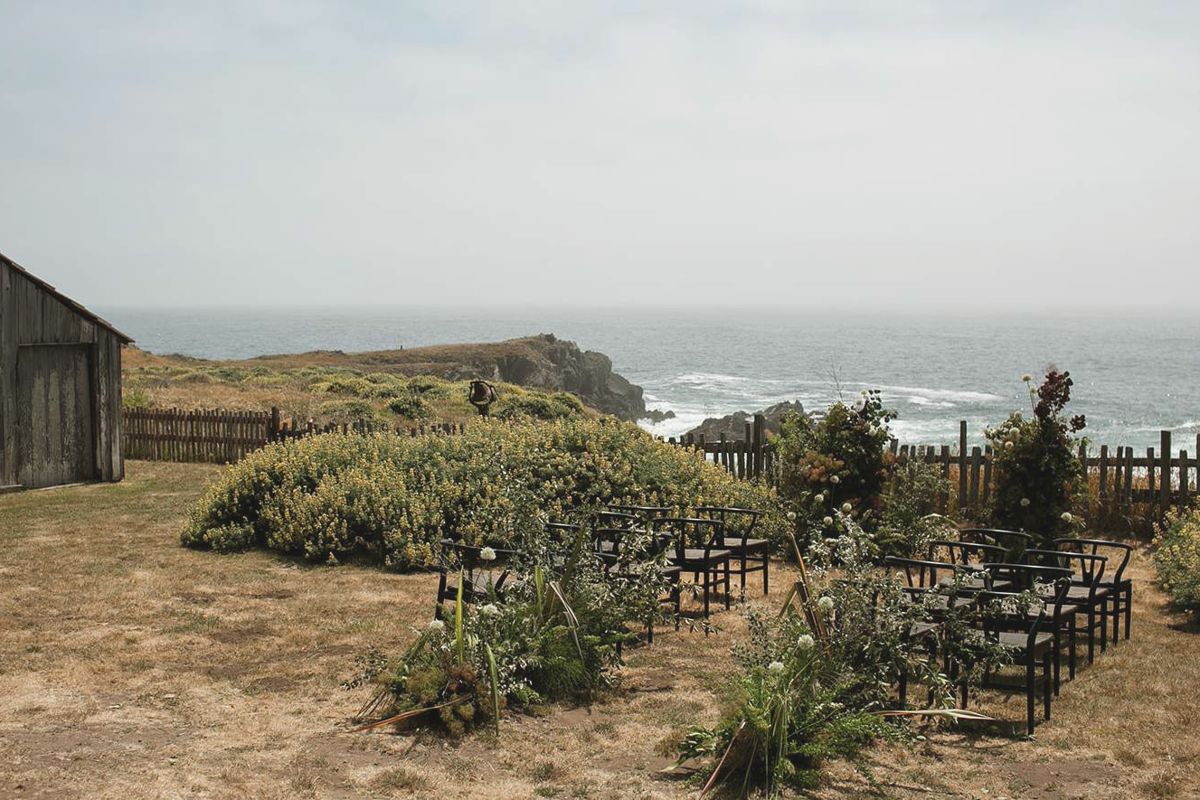 Ceremony chairs arranged in the Barn Meadow beside the weathered barn, ocean beyond the fence